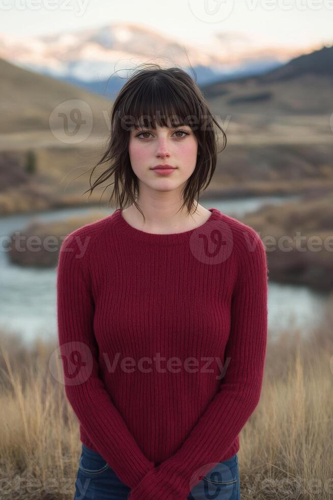 A woman in a red sweater stands in front of a river photo