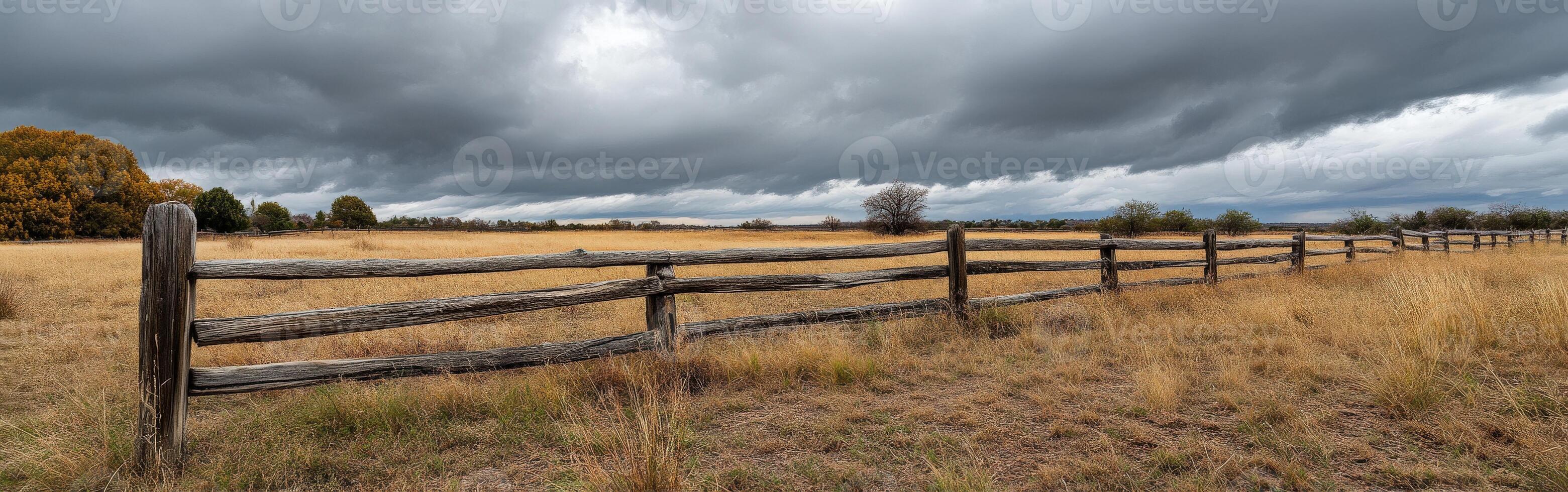 A fence in a field with storm clouds above it photo