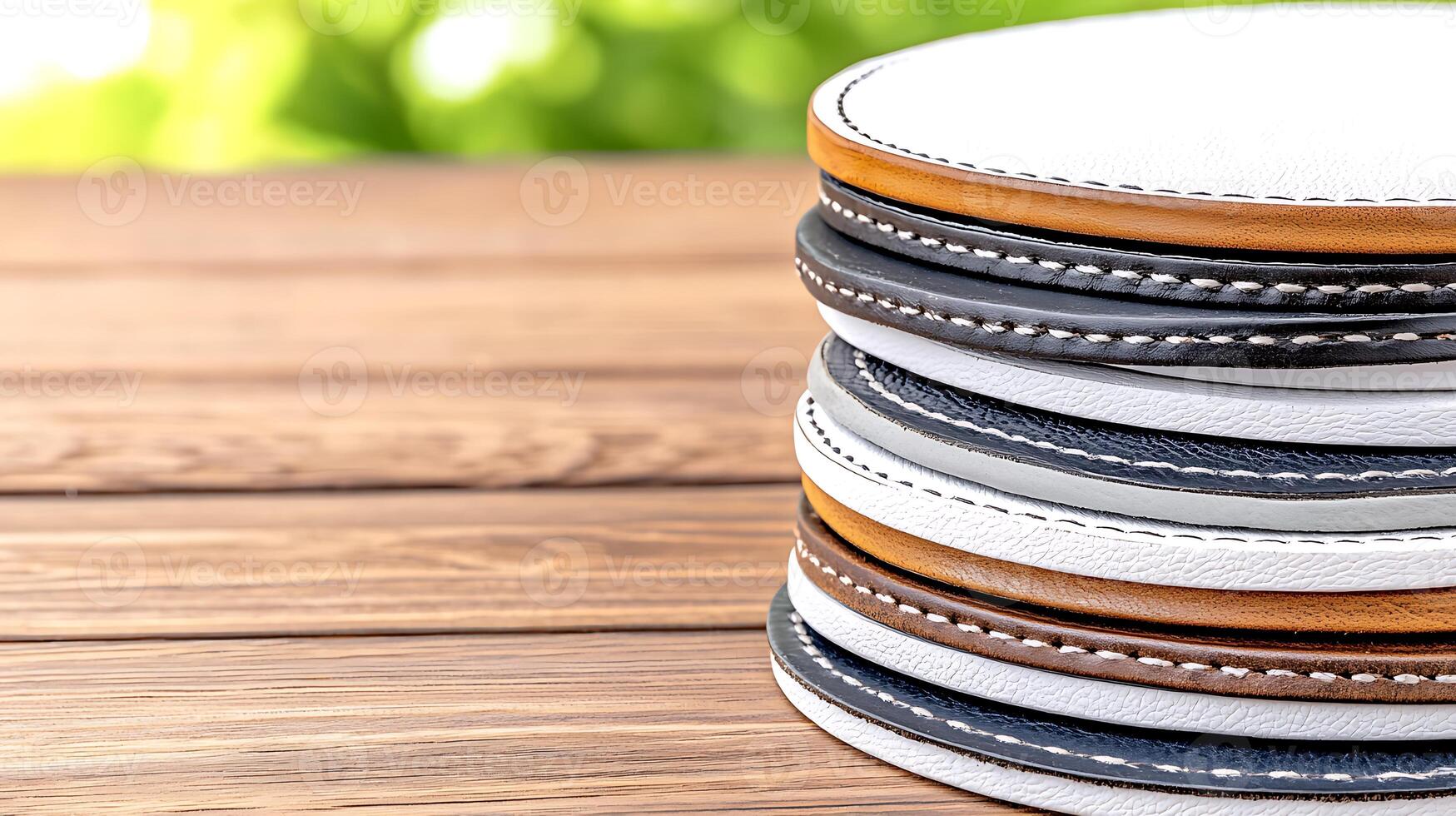 Stacked coasters in various colors resting on a wooden table with a blurred green background photo