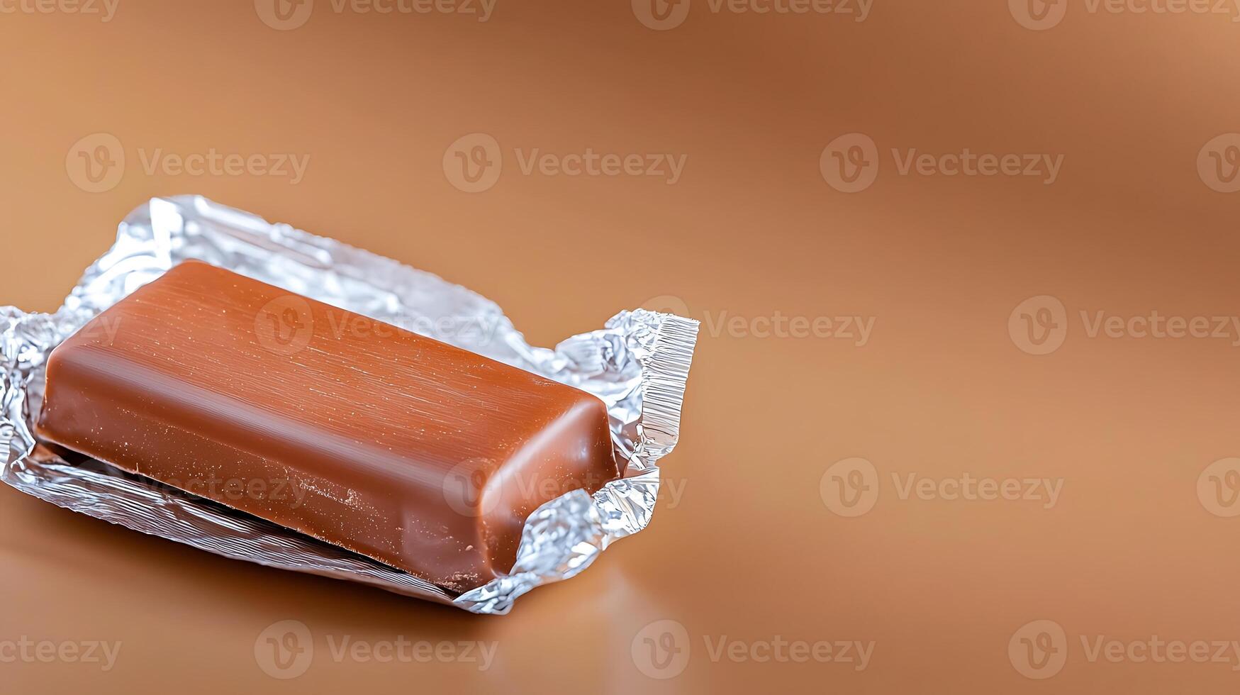 A close-up of a chocolate bar partially wrapped in foil on a smooth brown background photo