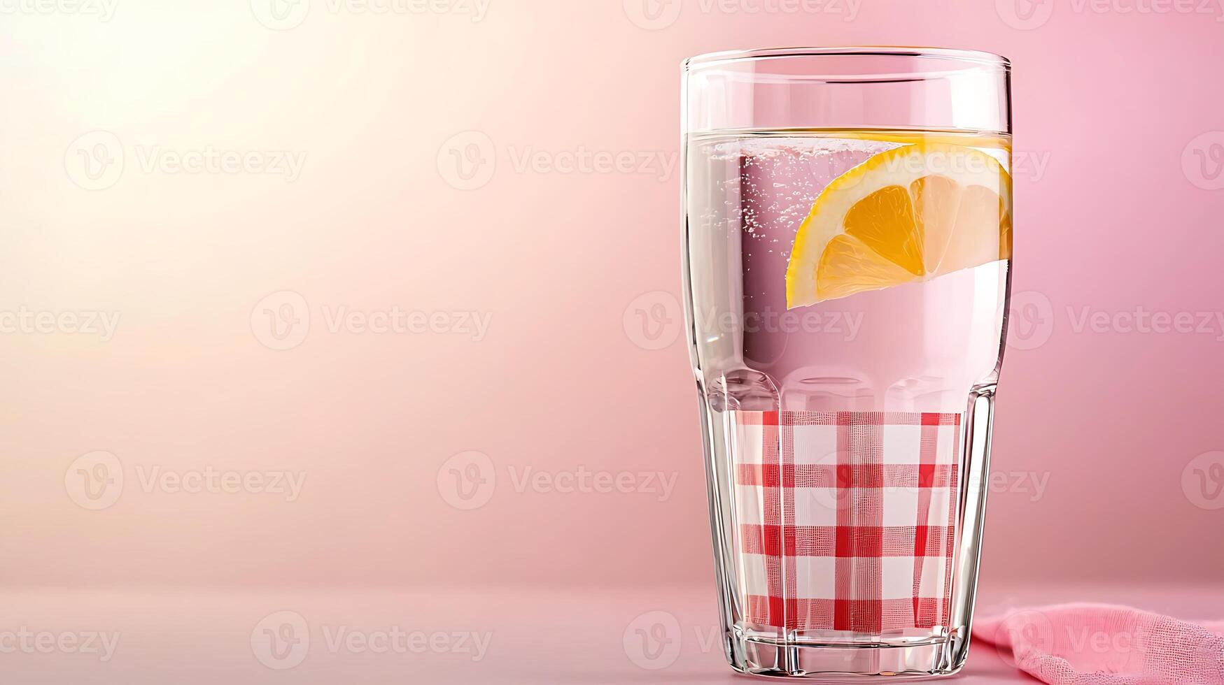 Refreshing glass of lemon water on a pink background with a checkered tablecloth photo