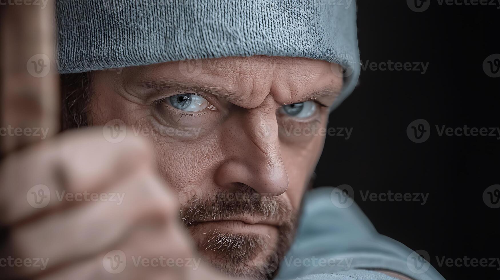 Intense close-up of a focused man aiming with a bow, showcasing determination in a dark setting photo