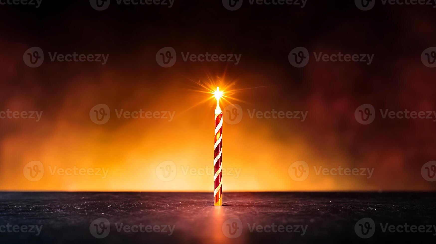 A single lit birthday candle on a dark table with a vibrant orange and red smoky background photo
