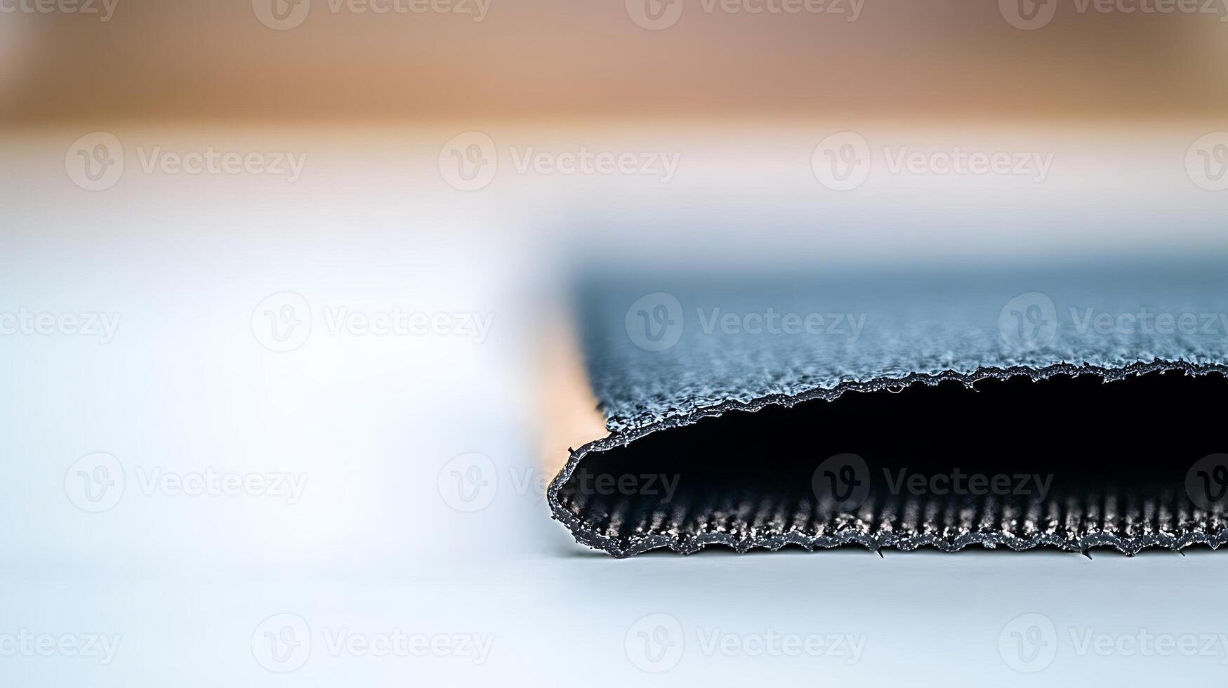 Close-up view of a textured fabric edge, showcasing its weave and color gradient against a blurred background photo