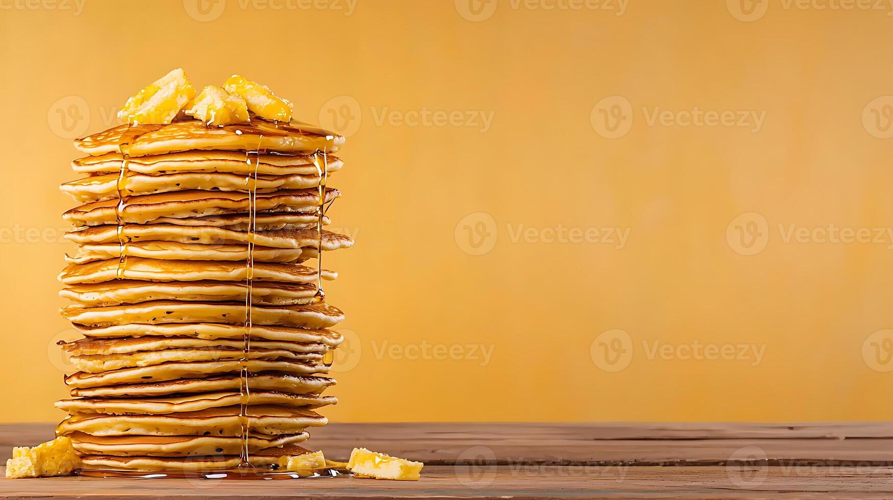 Stacked pancakes drizzled with syrup on a wooden table against a warm yellow background photo