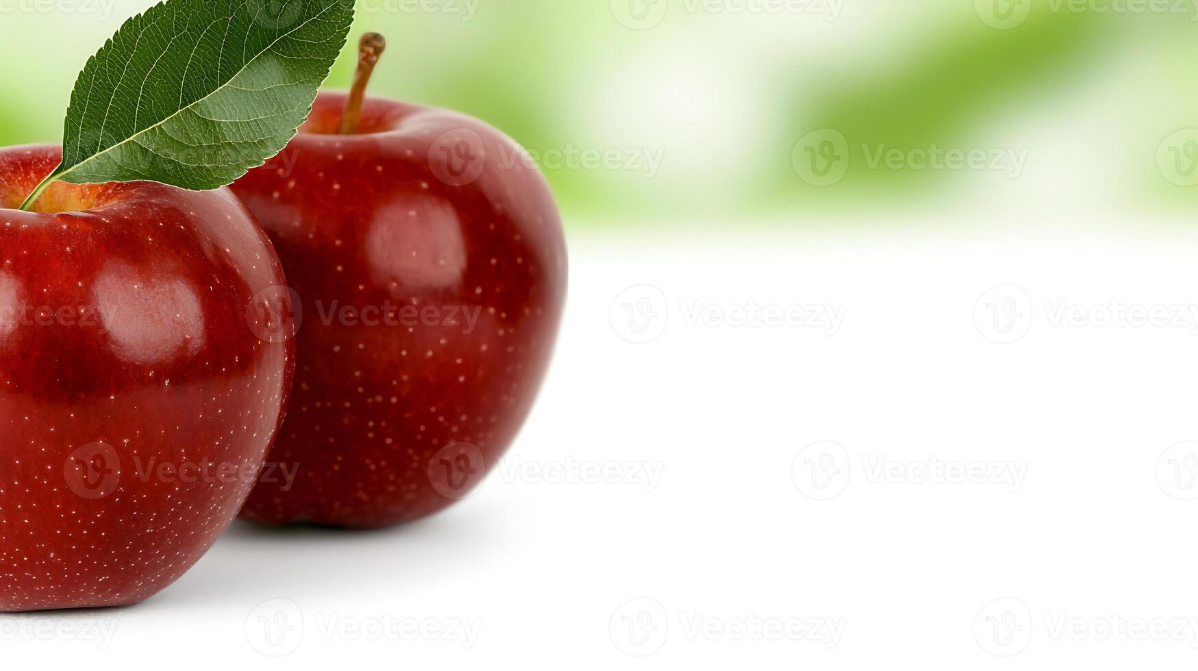 Two fresh red apples with green leaves, placed on a white surface with a blurred green background photo