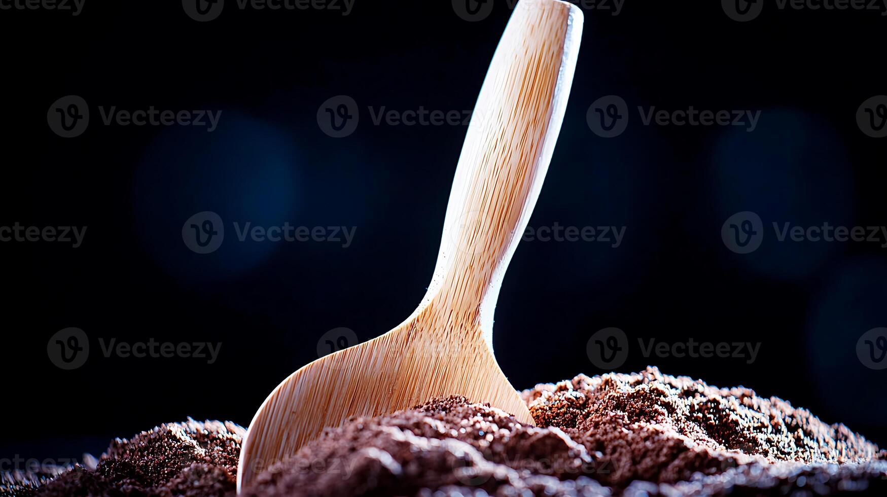 Wooden scoop resting in a mound of cocoa powder with a dark, blurred background photo