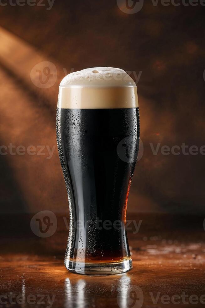 Cold glass of dark beer with foam on wooden table in warm light photo