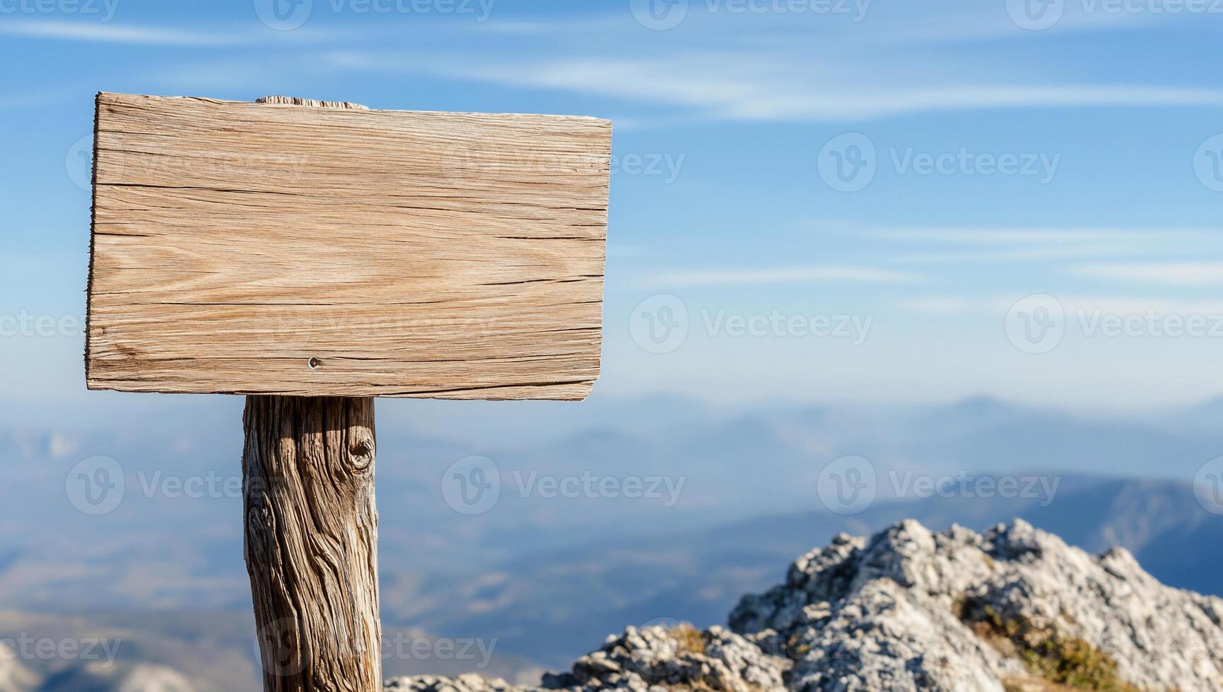 A wooden signpost stands on a rocky mountain peak against a blue sky. photo