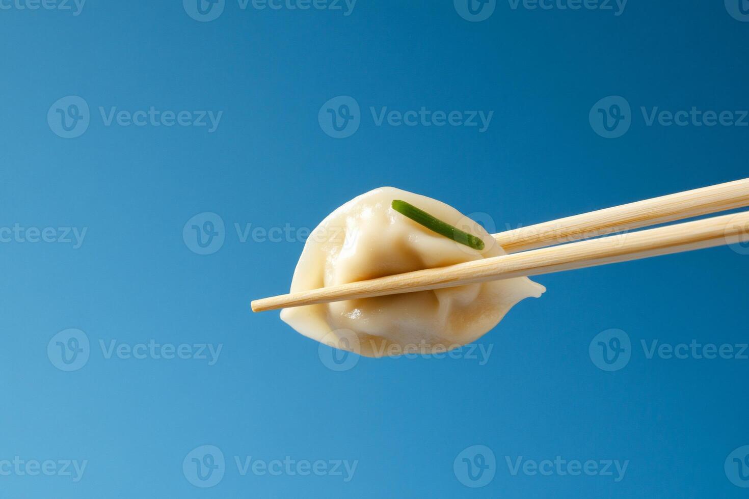 A dumpling held with chopsticks against a blue background. photo