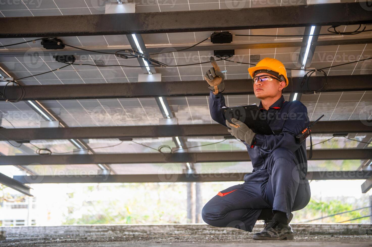 A solar panel installer points his finger at a faulty power line and notes it on a clipboard. photo
