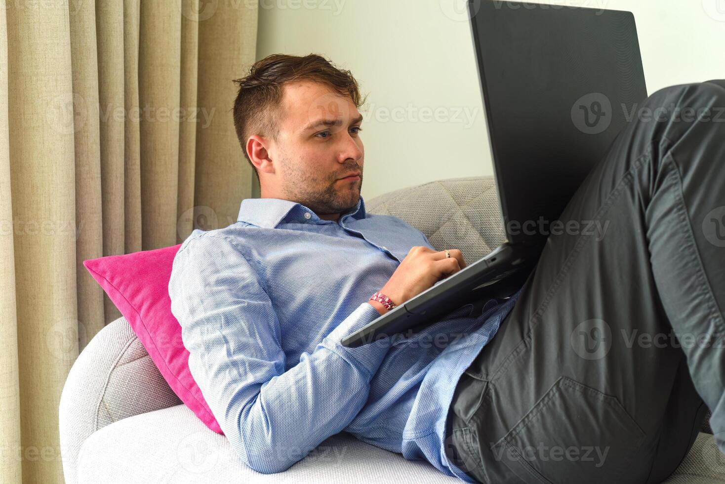 Young man freelancer working from home with his laptop laying on couch photo