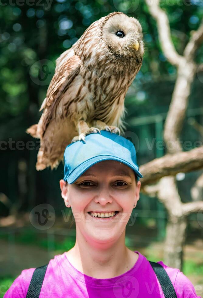 Portrait of laughing 36 years old Russian woman with Ural owl Strix uralensis bird sitting on her head close up photo