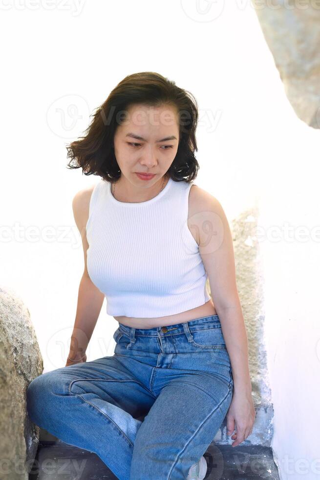 Vietnamese young woman in blue jeans and a white t-shirt looking down photo