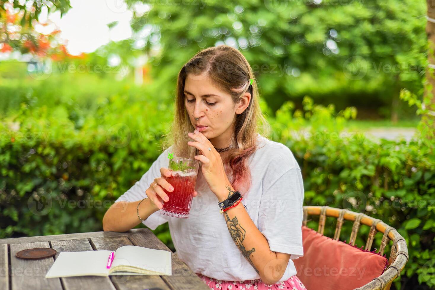 Cute woman sitting on a chair in summer garden, drinking ice tea and writing in a notebook photo