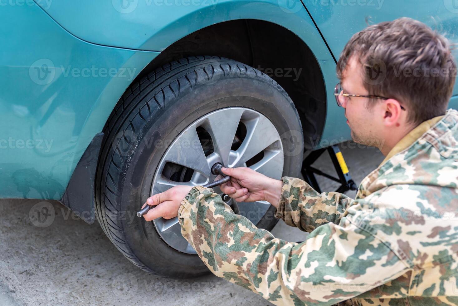 young russian man changing car tire for winter tires photo