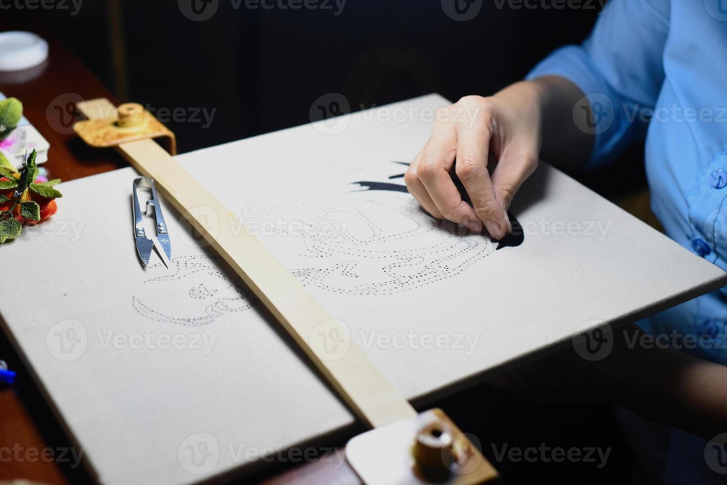 Hand of vietnamese woman embroiders a picture with a needle and silk threads through pre-punched holes photo