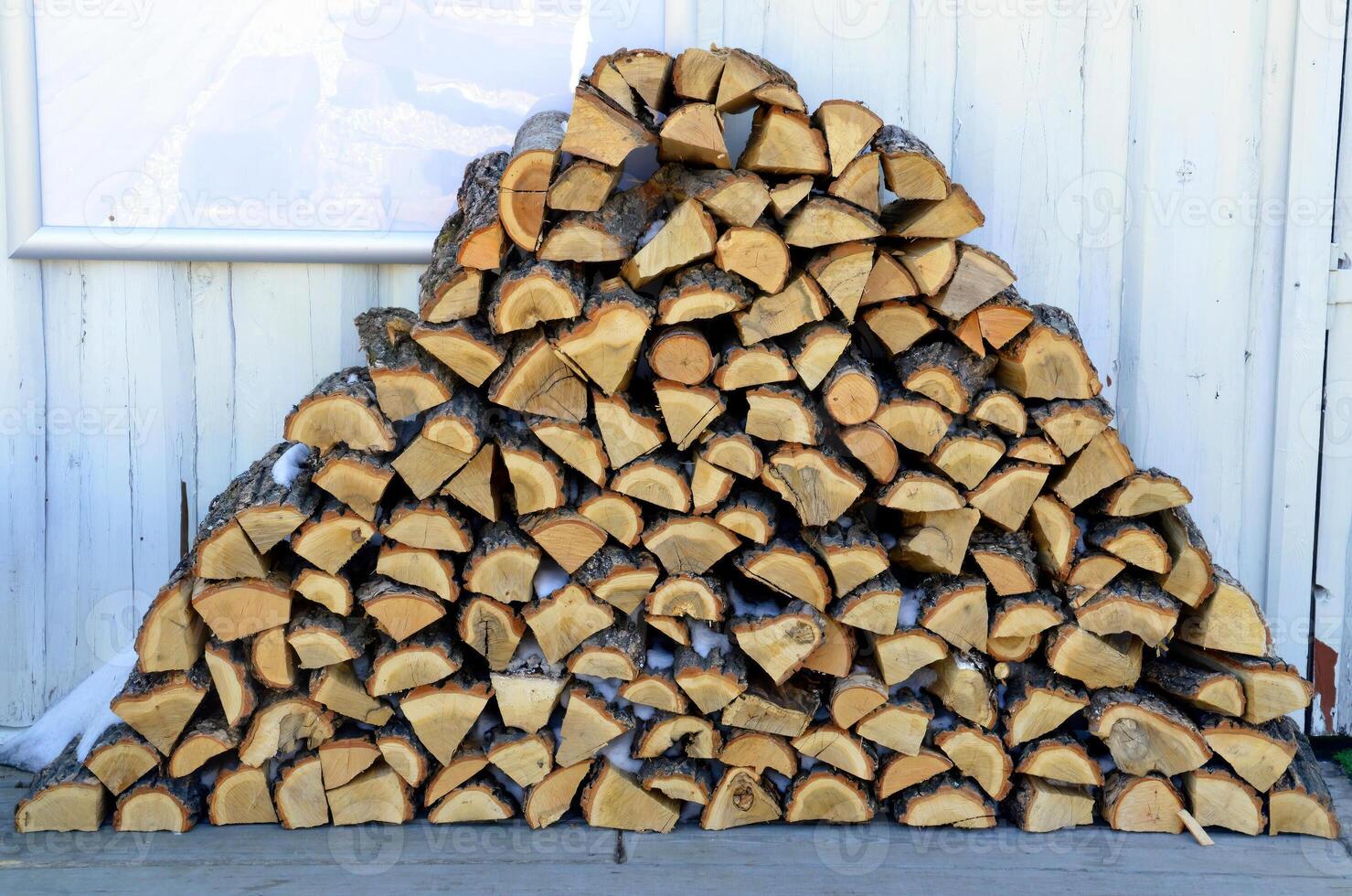 stacked pile of firewood with snow on a white wall background photo