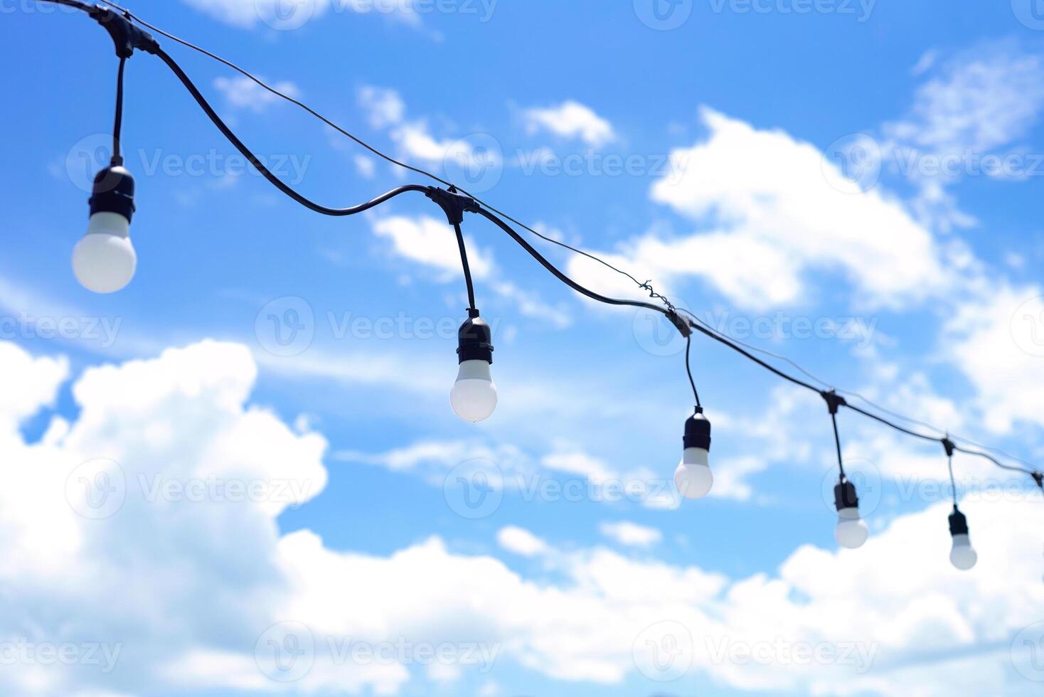 a lot of light bulbs hanging against a blue sky with clouds photo