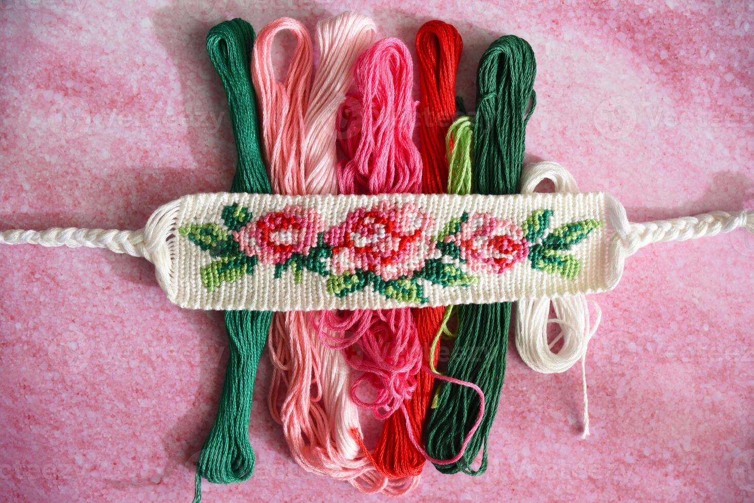 Woven DIY friendship bracelet with bright flower pattern Rose near scissors and skeins of embroidery thread photo