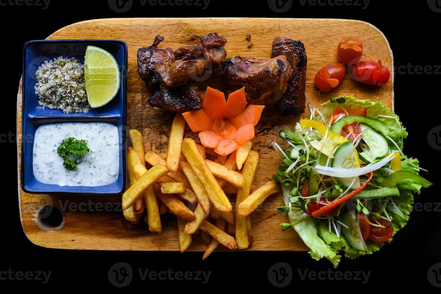 Grilled smoked pork ribs with french fries and sauces on wooden board on black background side view photo