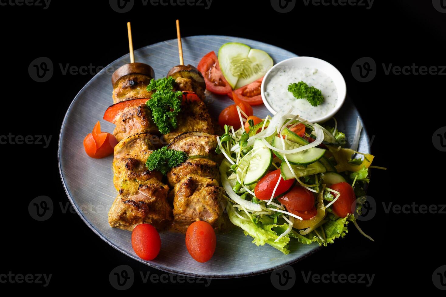 Pork skewers with grilled vegetable served with salad on black background top view photo