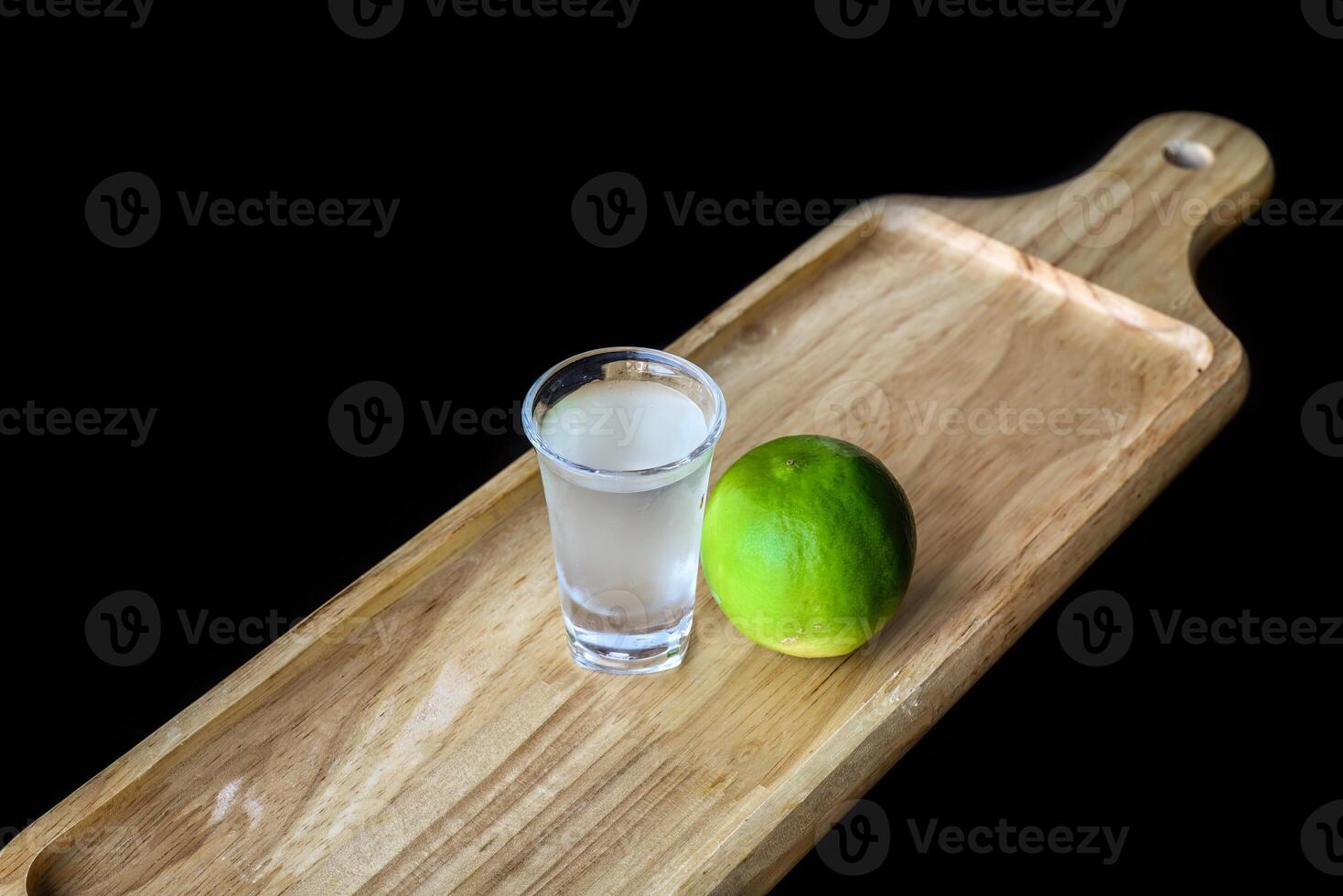Alcohol shot made of lime juice on wooden board with with copy space photo