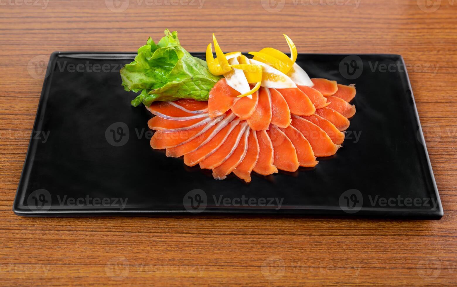 slicing appetizer of red fish slices on a black plate on a wooden table top view photo