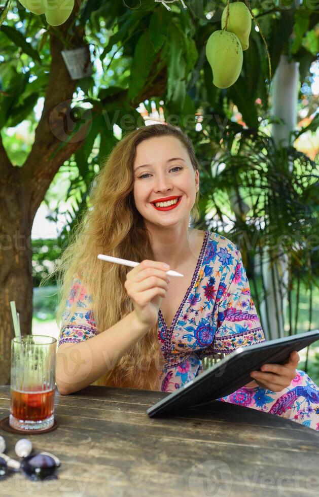 Beautiful woman artist and illustrator drawing, sitting by the table with electronical tablet and stylus photo