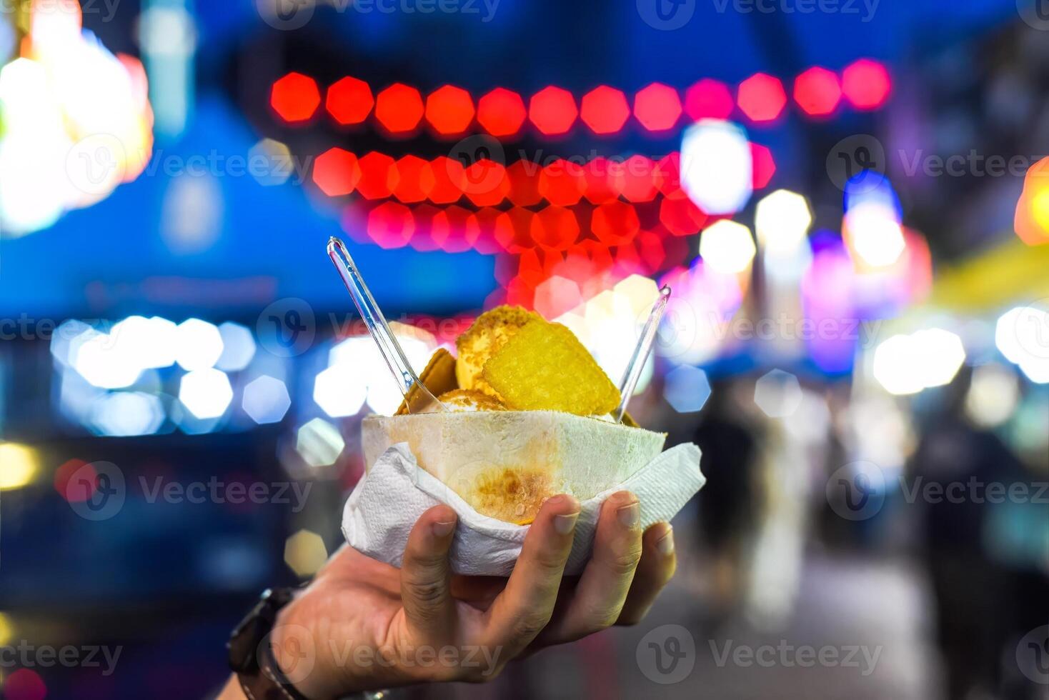 Hand holding coconut and mango ice cream in coconut shell against lights of Jalan Alor street food market in Kuala Lumpur photo