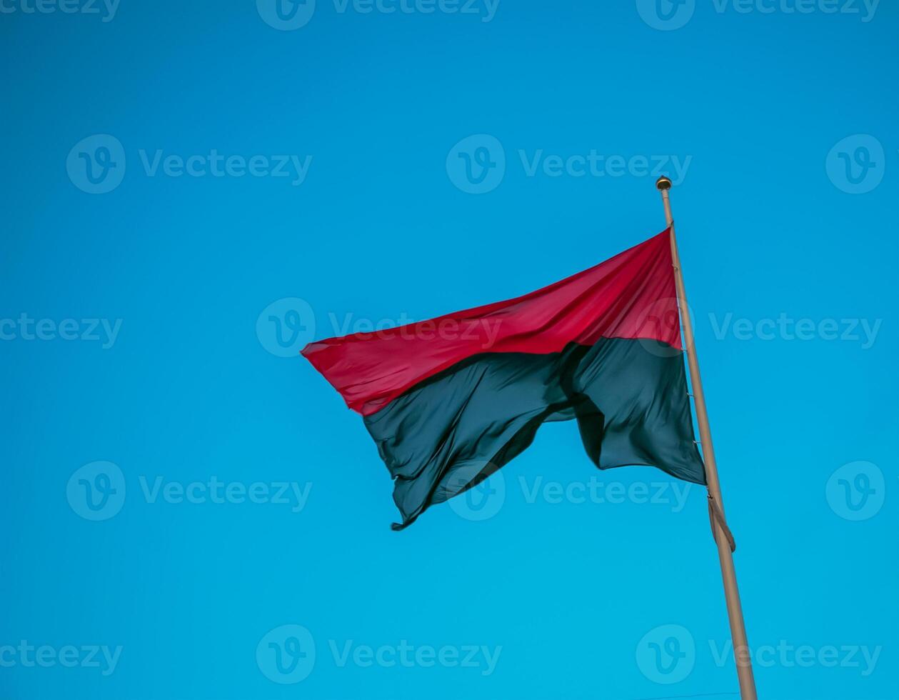 Red-black flag of Ukrainian nationalists, isolated on blue sky background, close-up. Background of silk fabric fluttering in the air. photo
