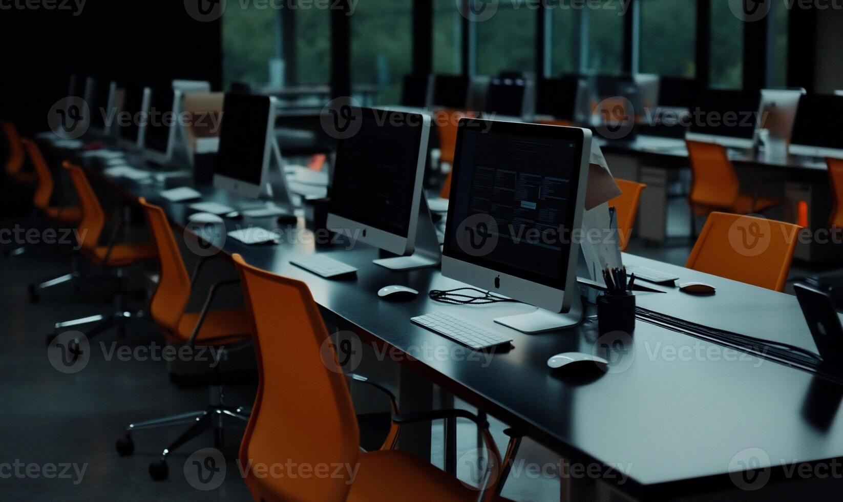 Modern computer lab with many desks and chairs. Rows of computers, dark tables, and bright orange chairs photo
