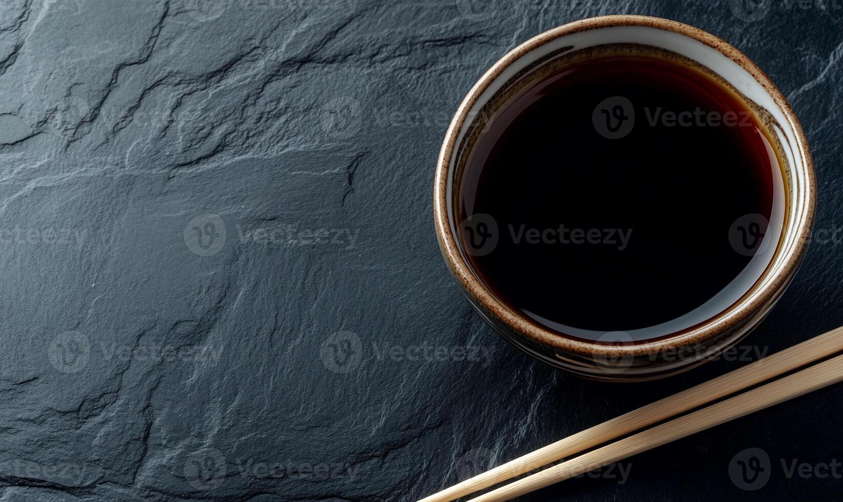 Dark soy sauce in a small bowl on a dark slate surface with chopsticks photo