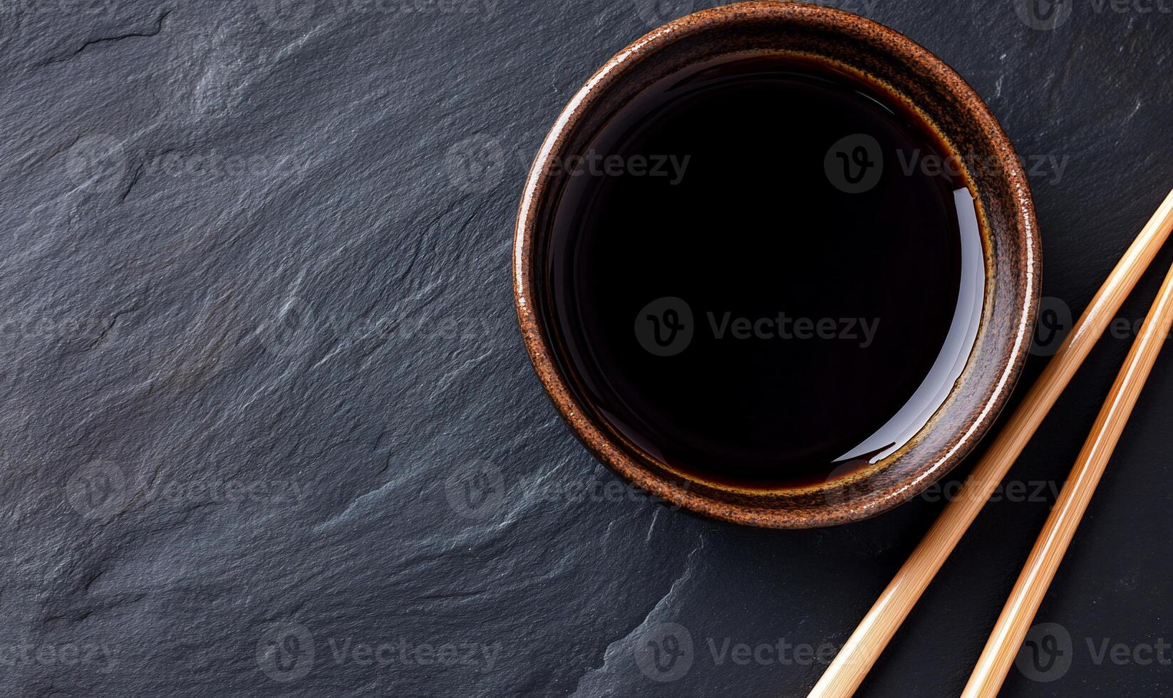 Dark Soy Sauce in Small Bowl with Chopsticks on Dark Stone photo