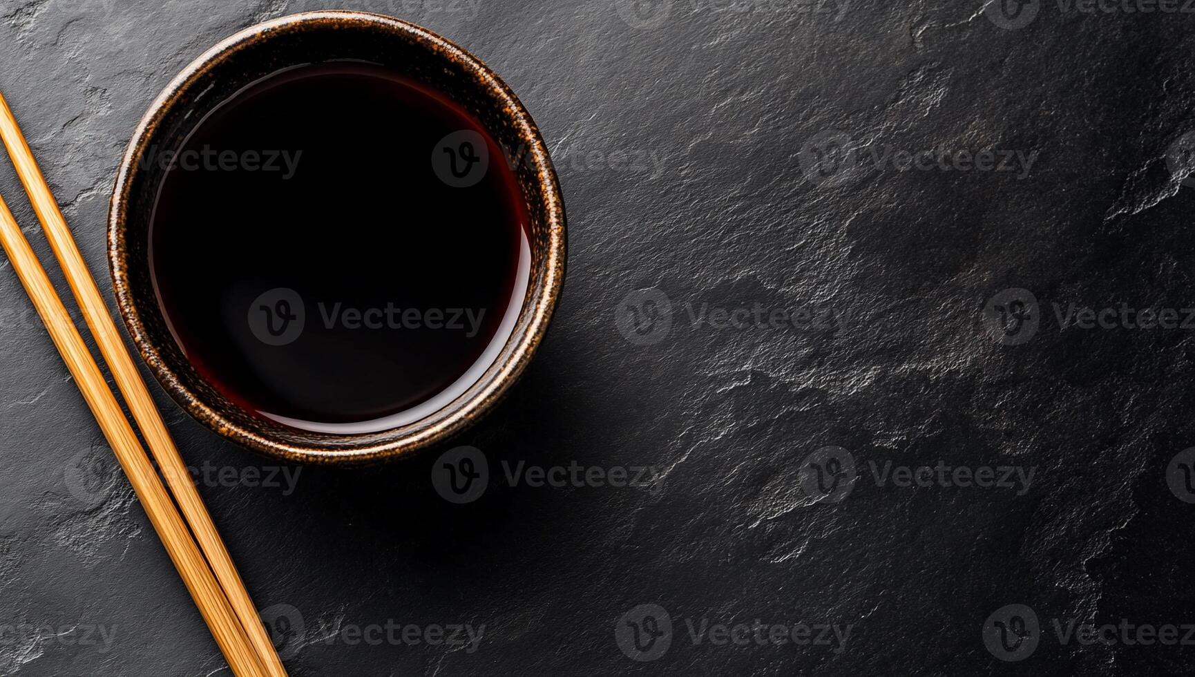 Dark soy sauce in bowl with chopsticks on a dark stone surface photo