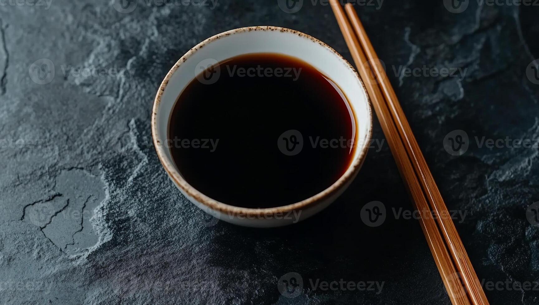 Soy Sauce in small bowl with chopsticks on dark stone surface photo
