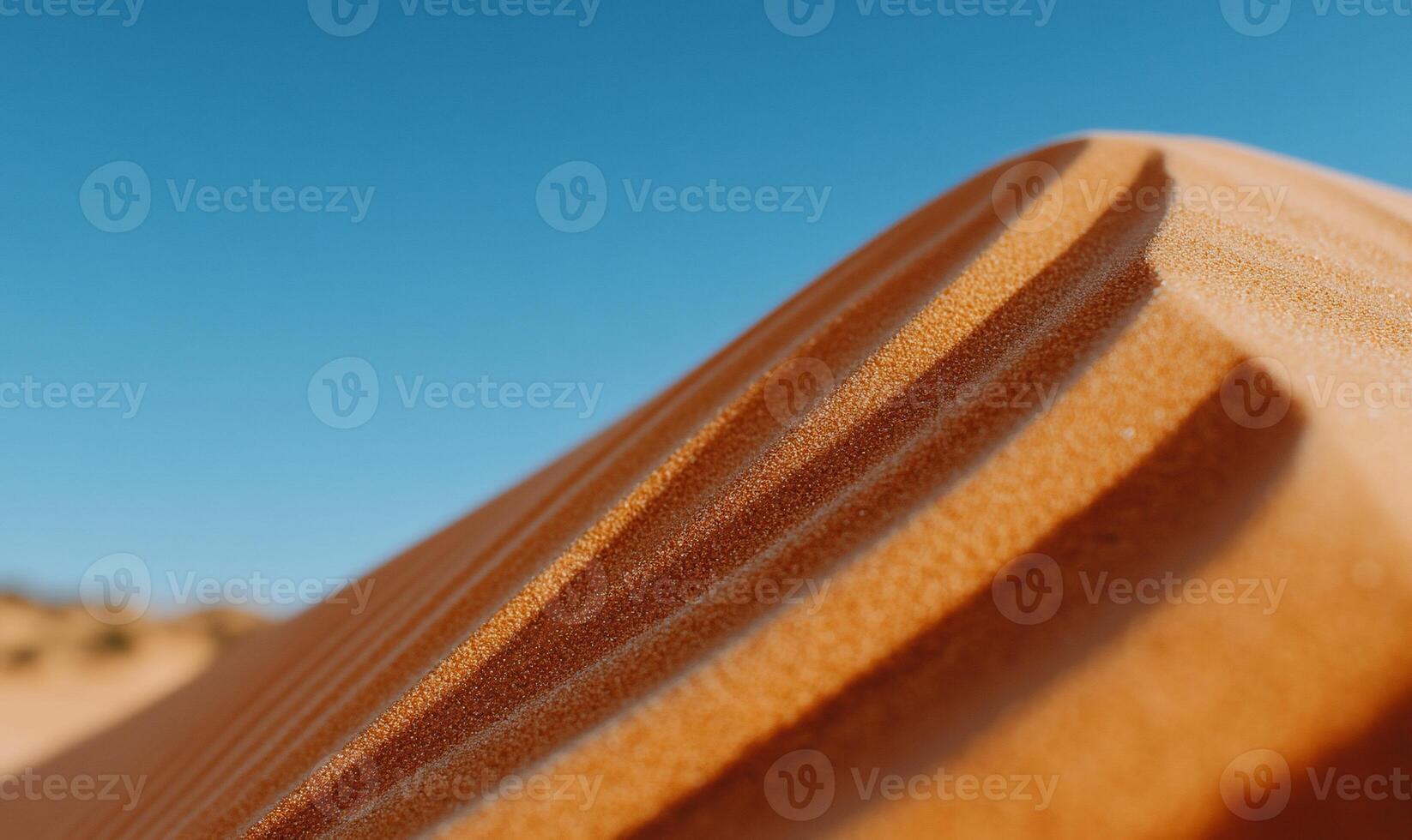 Sunlit sand dune with ripple patterns under a clear blue sky photo