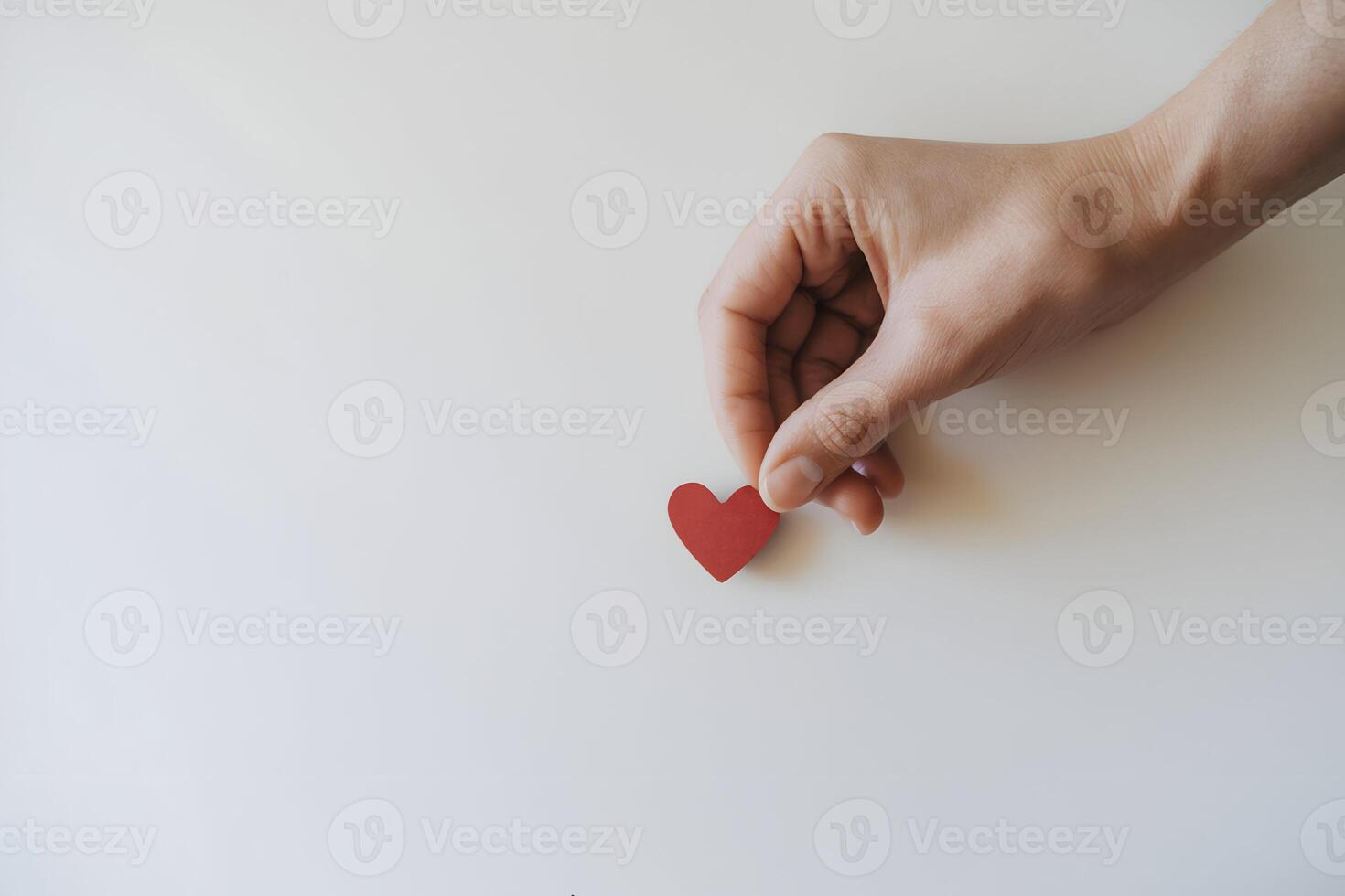 Hand holding a red heart shaped object against a white background photo