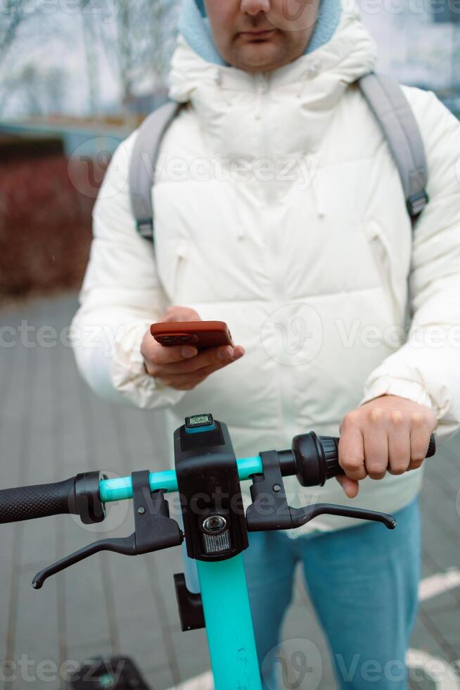 Handsome man using smartphone app. Guy approaches an electric scooter and using mobile phone app NFC contactless locker on bike bicycle in sharing parking lot. photo