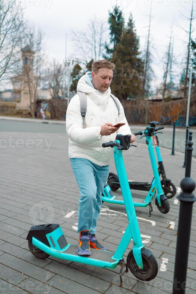 Caucasian man using smartphone app. Male approaches an electric scooter and using mobile phone app NFC contactless locker on bike bicycle in sharing parking lot. Ecological transportation photo