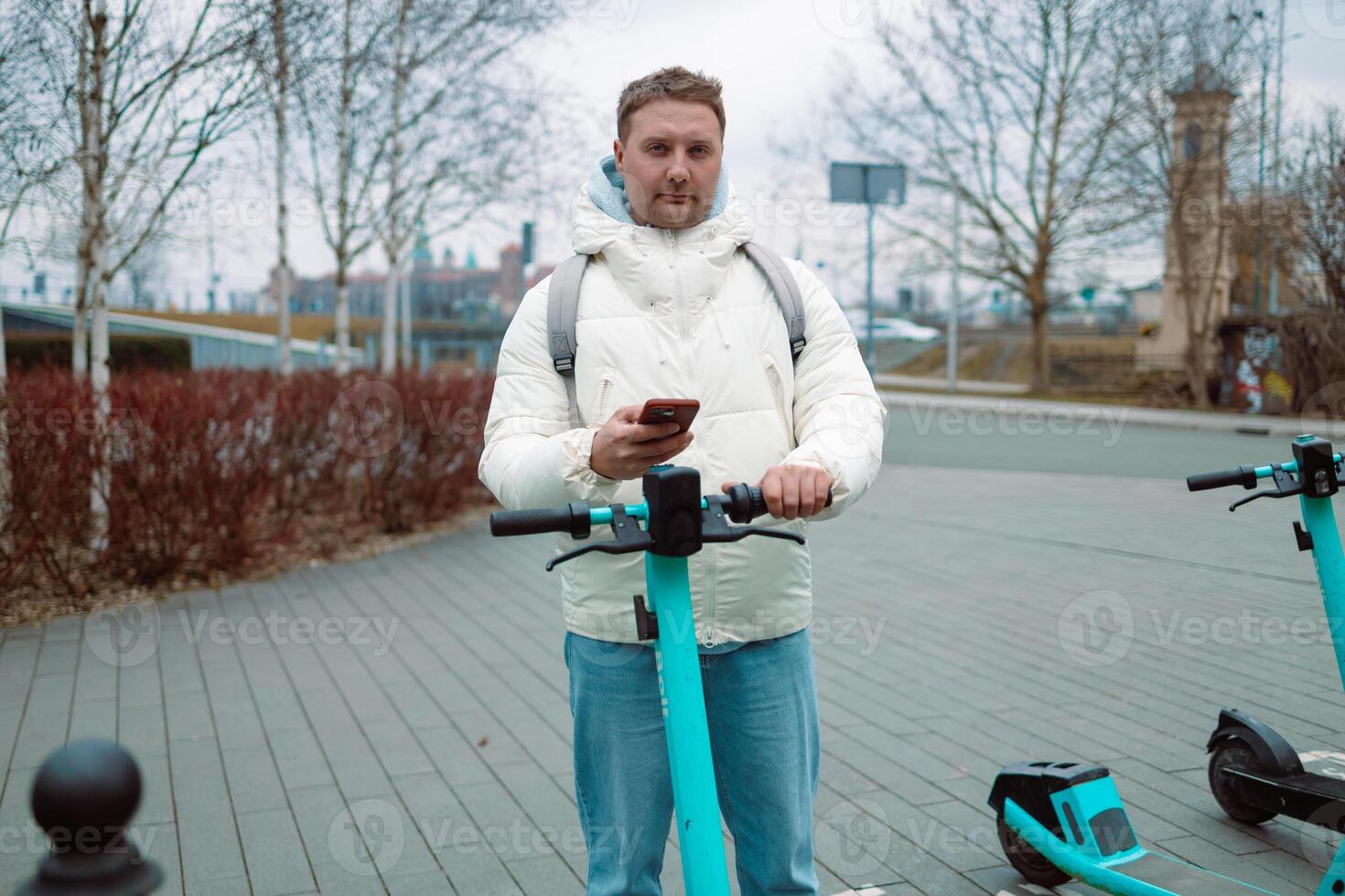 Handsome man using smartphone app. Guy approaches an electric scooter and using mobile phone app NFC contactless locker on bike bicycle in sharing parking lot. photo