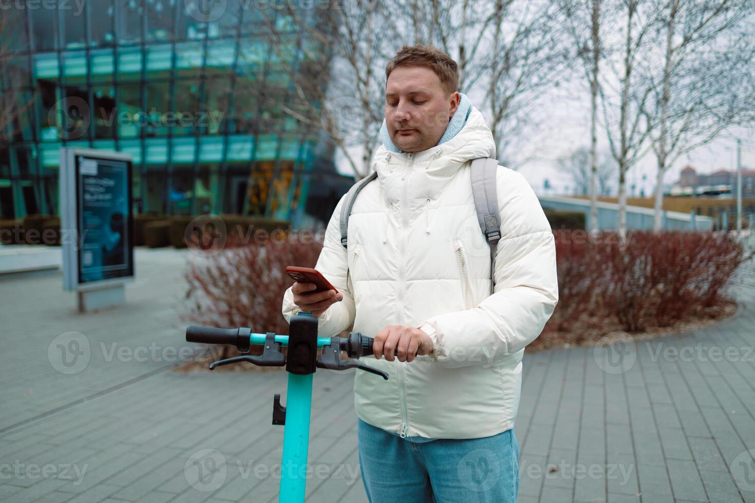 Handsome man using smartphone app. Guy approaches an electric scooter and using mobile phone app NFC contactless locker on bike bicycle in sharing parking lot. photo
