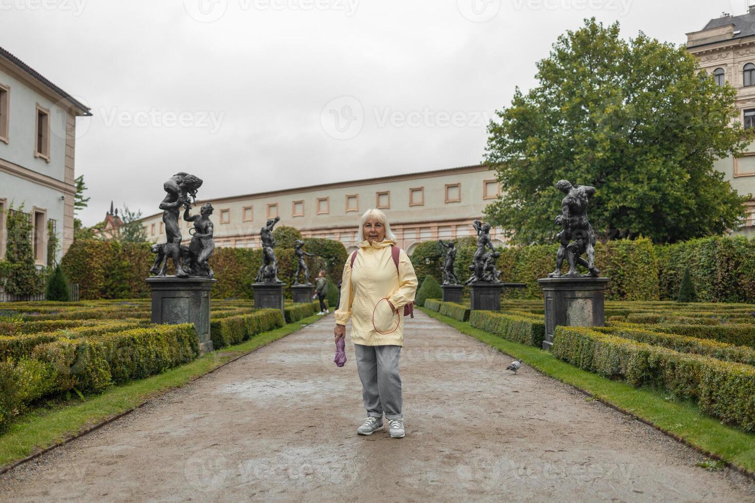 A female tourist walks around along a decorative alley decorated with many statues in a decorative park at Wallenstein Palace building in Prague in Czech Republic photo