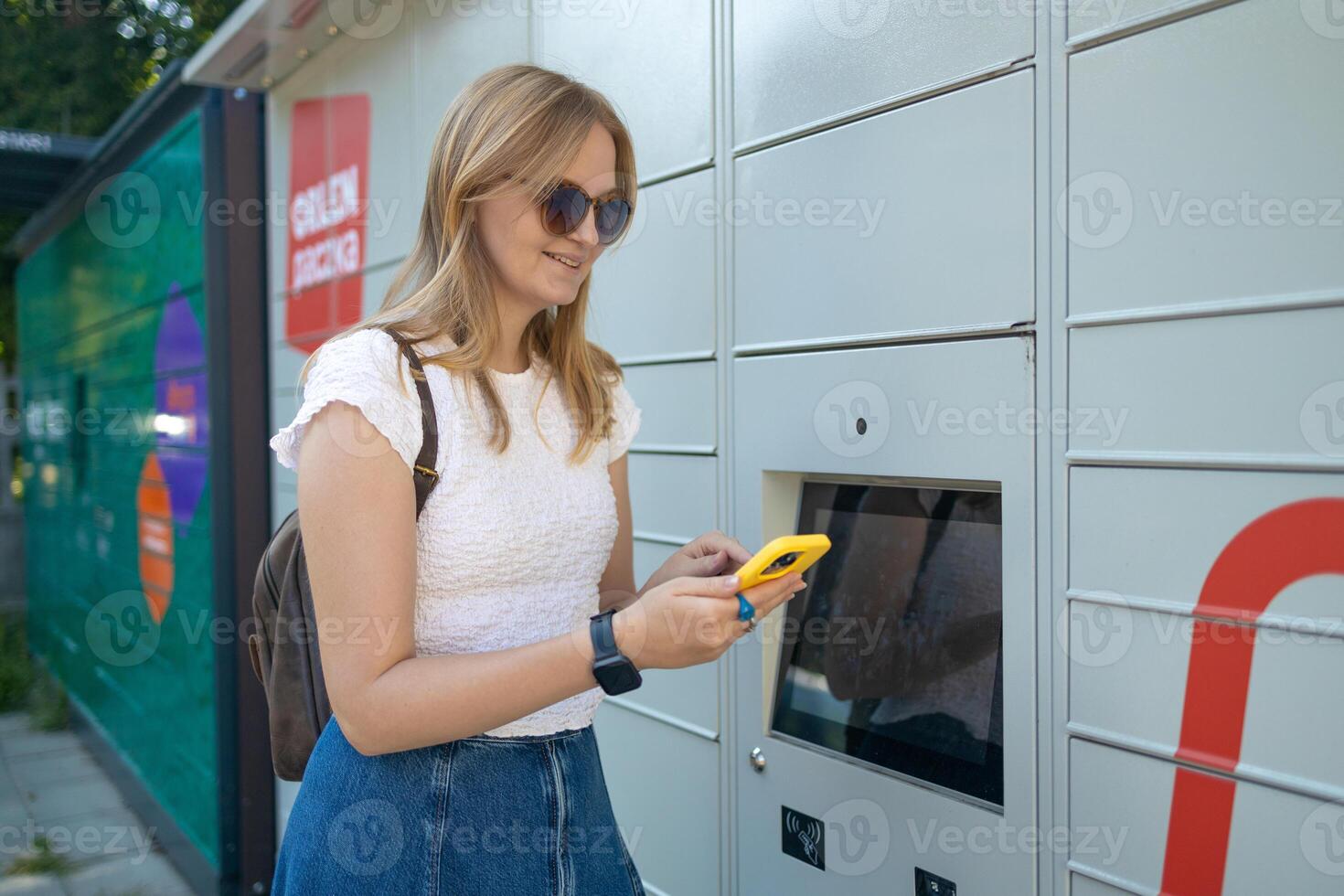 Woman using automated self service post terminal machine or locker to deposit the parcel for storage photo