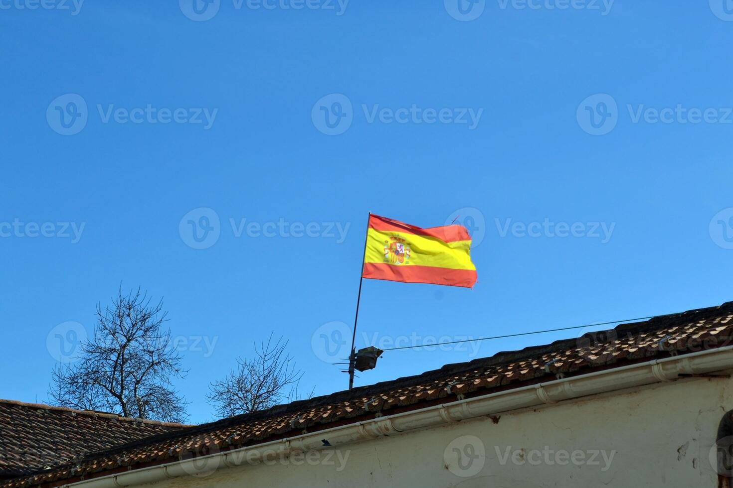 Spanish flag waving on rooftop against clear blue sky. National day of Spain photo