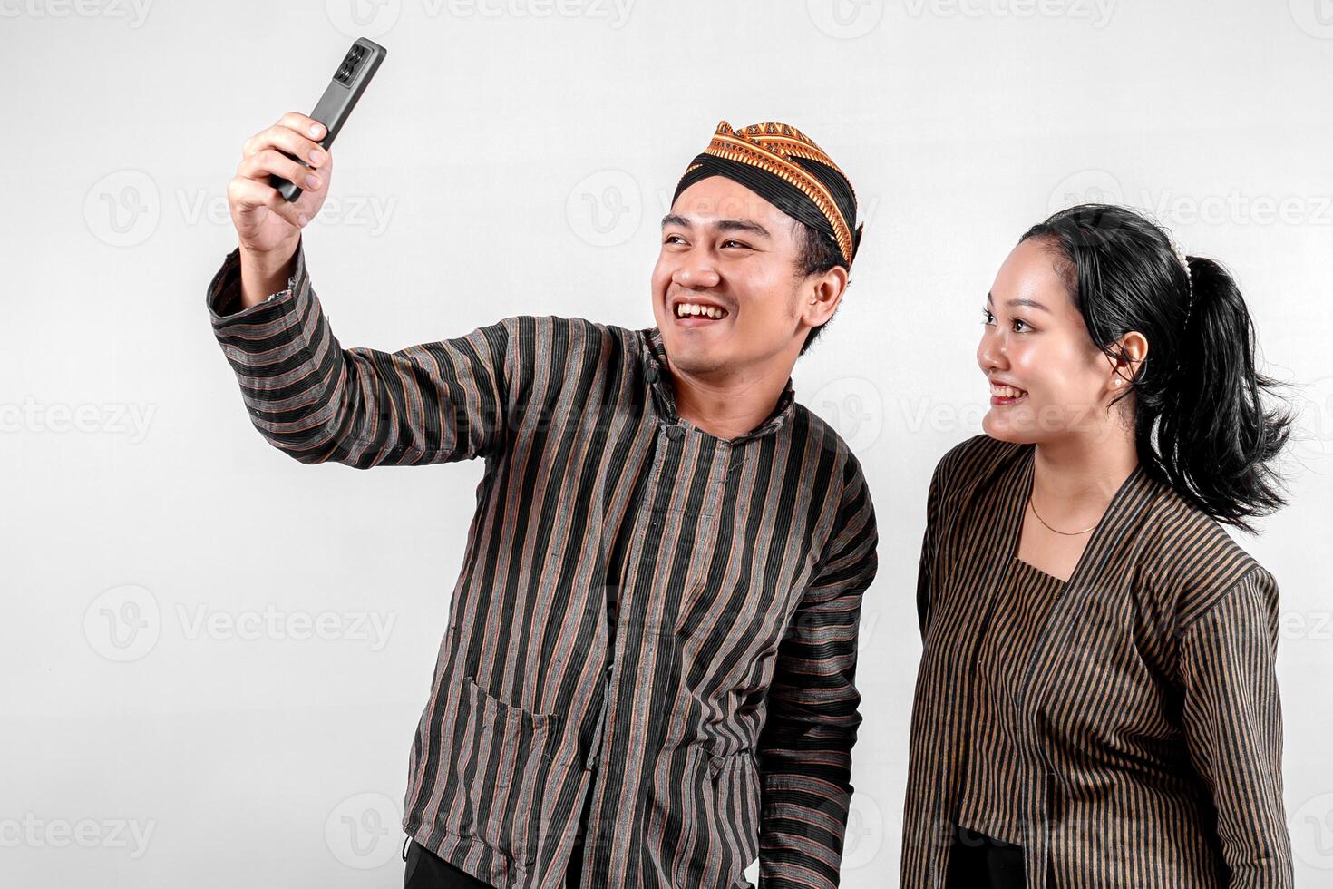 a Indonesian couple wearing traditional Javanese Lurik or Sorjan clothing, smiling while taking a selfie. Symbol of heritage, joy, and togetherness. Isolated on white background. photo