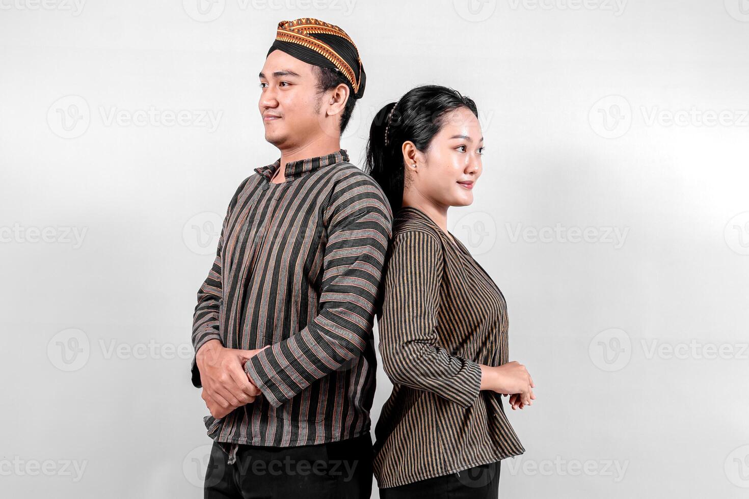 An Indonesian man and a woman stand confidently back to back, wearing traditional lurik attire, exuding pride and happiness photo