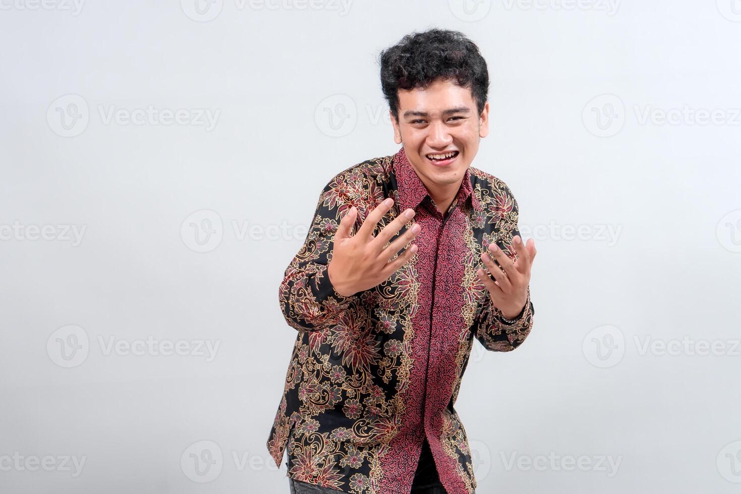 A young man joyfully poses in a traditional batik shirt, showcasing vibrant patterns and a cheerful expression against a neutral background. photo