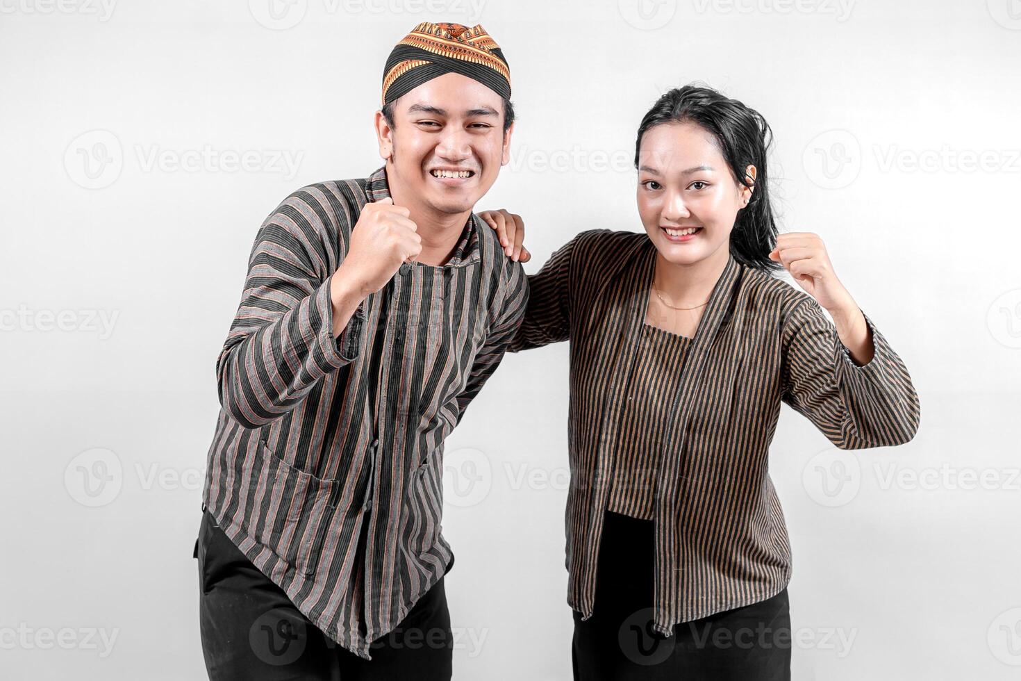 Indonesian couple wearing traditional Javanese Lurik or Sorjan clothing, smiling with fists raised. Cultural striped outfit, symbolizing heritage and resilience. Isolated on white. photo