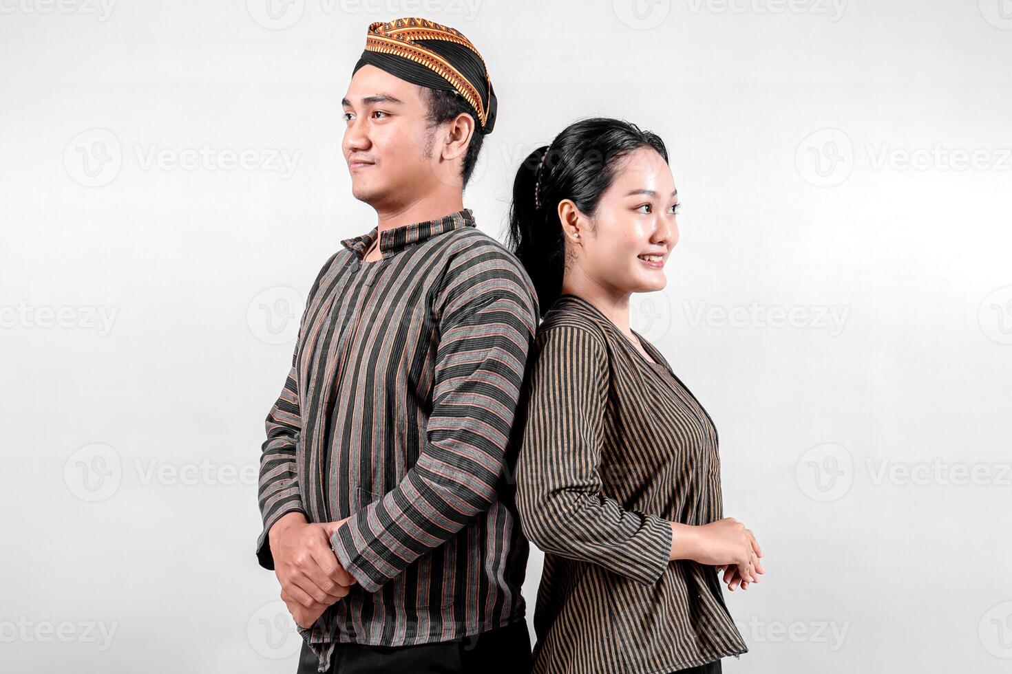 An Indonesian man and a woman stand confidently back to back, wearing traditional lurik attire, exuding pride and happiness. photo